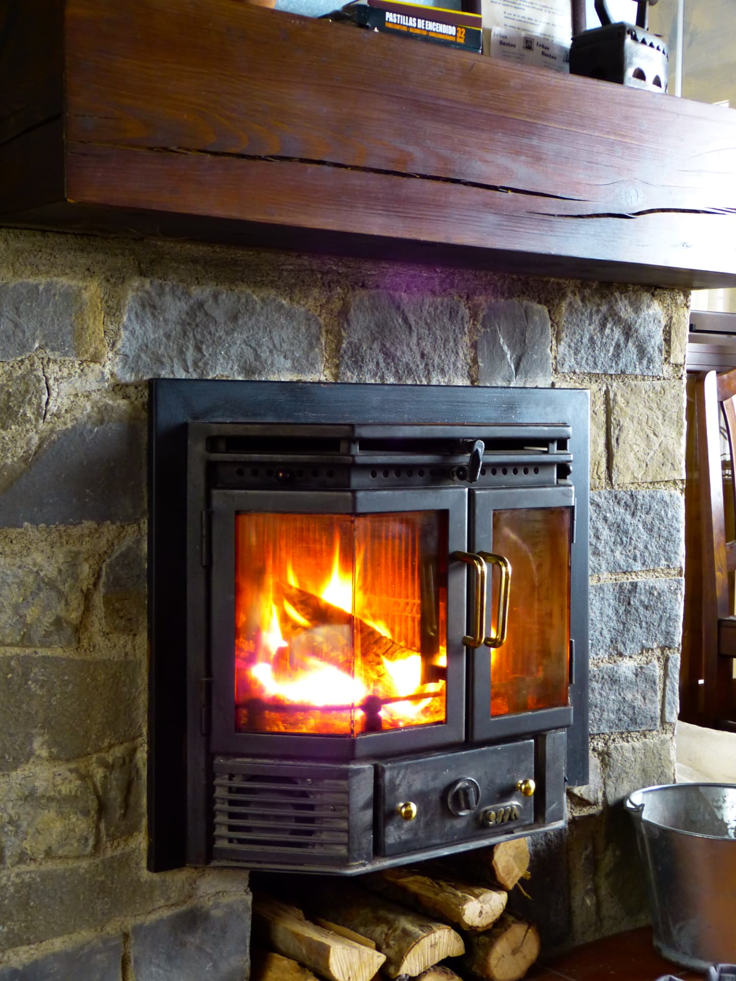 Chimenea de leña encendida sobre muro de piedra en el salón de Casa Artena